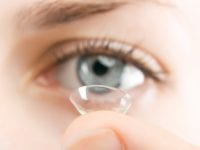 Beautiful young woman inserting a lens into her blue eye, studio shot.